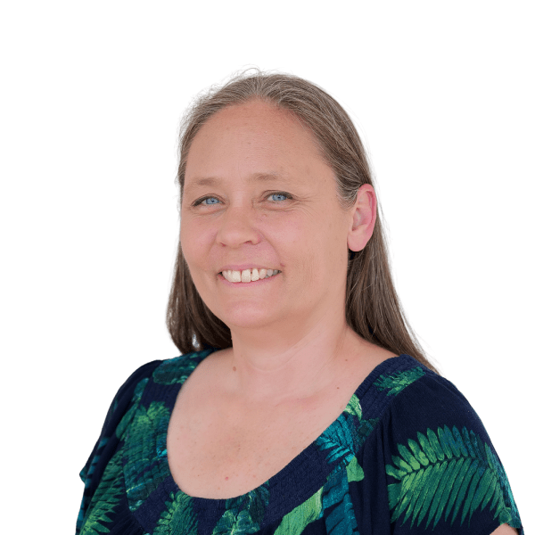 A woman with long brown hair and blue eyes is smiling, wearing a navy blue top with a green leaf pattern, against a plain white background.